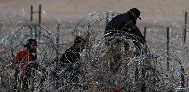 Migrantes intentan cruzar la cerca de alambres en la frontera que divide a México de EU