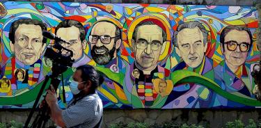 Un camarógrafo camina el 6 de enero de 2022 frente a una pintura en San Salvador dedicada a San Óscar Romero y seis sacerdotes jesuitas asesinados el 16 de noviembre de 1989.