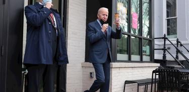 El presidente de EU, Joe Biden, saluda a periodistas alzando un heladito durante un paseo por Washington D.C., este martes 25 de enero.
