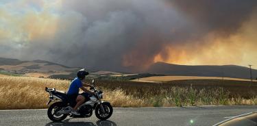 Una persona circula en moto este sábado 18 de junio de 2022 en la localidad de Astráin, Pamplona, España, desde donde se puede apreciar un incendio.