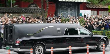 El coche fúnebre con los resto de Shinzo Abe pasa frente a una multitud a la entrada del templo budista de Tokio