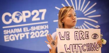 Activista con un cartel en la cumbre del clima que avisa a los representantes de los países que están siendo observados