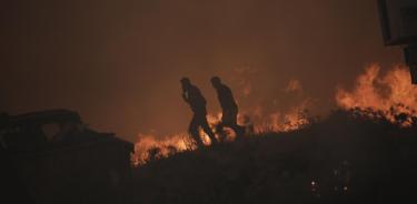 Un bombero junto a un vecino tratan de extinguir las llamas de un incendio en Atenas