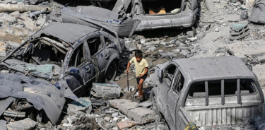 Un niño pasa junto a coches destruídos tras los ataques aéreos israelíes en Gaza
