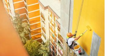 Pintor recubriendo el exterior de un edificio con pintura amarilla
