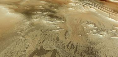 esta imagen rectangular muestra parte de la superficie marciana como si el espectador estuviera mirando hacia abajo y a través del paisaje, con el suelo irregular y moteado apareciendo en tonos arremolinados de marrón y tostado.