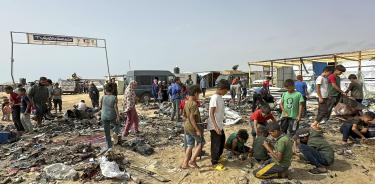 Niños entre los restos calcinados del campamento de refugiados en Rafah, incendiado tras el ataque israelí del domingo