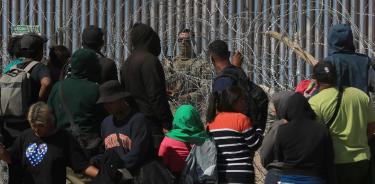 Migrantes esperan entre los alambres de púas mientras un agente estadounidense vigila en Ciudad Juárez, Chihuahua