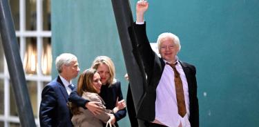 Assange alza el puño a su llegada al aeropuerto de Camberra, mientras su esposa Stella se abraza con la abogada del fundador de Wikileaks