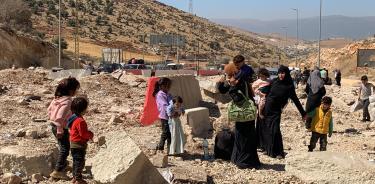 Mujeres con bebés a cuestas y padres con atados en la cabeza atraviesan como pueden el polvoriento cráter que dejó un reciente bombardeo israelí en el principal paso fronterizo entre el Líbano y Siria. EFE